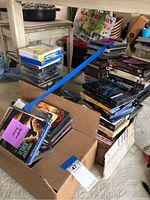 Multiple stacks and box of DVDs including superhero, kids DVDs with toys, and assorted series and movie titles.