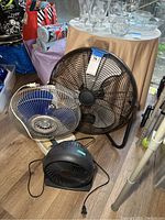 3 electric fans: large black Tatung oscillating fan, medium blue fan, and small black Honeywell fan, shown on floor with table and glassware in background