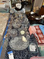 Top view of multiple pieces of clear glassware including bowls, trays, candy dishes, and candleholders arranged on a blue patterned cloth.