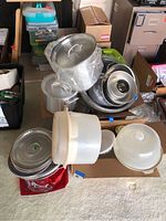 Overview photo showing various kitchen items including Dutch ovens, trays, cake holders, and Tupperware stacked in a box.