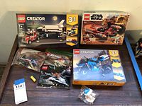 Photo showing 6 LEGO sets including Creator shuttle truck set 31091 with 341 pieces, Creator superbike 31114 with 236 pieces, a Star Wars set with speeder bike and minifigures, several unopened plastic bags of LEGO Star Wars parts, and a sealed blue and white robot minifigure labeled Galaxy.
