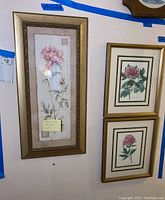 Full view of three framed rose motif wall art pieces on white wall with blue tape marks.