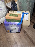 Singer portable sewing machine with Sew D'Lite labeling, cardboard box for Singer buttonhole attachment, purple Sew D'Lite machine box.