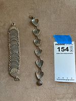Two bracelets laid flat: a linked coin sterling silver bracelet and a leaf motif bracelet, showing their design and length.