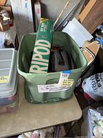 Plastic bin on table containing a green and yellow Ripod tripod box and camera bags.