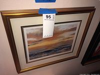 Framed landscape print showing sunset over water with a bronze frame and label 95 attached.