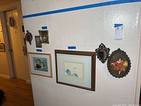 Wide view of six pieces of framed wall art and mirrors hung on a white wall, varying in sizes and styles.