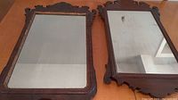 Two antique Chippendale style mirrors placed side by side on a table showing aged wooden frames and glass condition