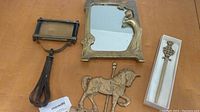 Photo showing the vintage brass hand mirror, brass mirror with female figure, brass horse wall hook, and boxed brass letter opener.