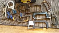 Overview of assorted clamps including various sizes of C clamps, vice clamps with blue handles, and slide clamps shown on a carpeted floor.