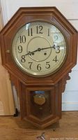 Full view of the wooden wall clock showing the octagonal frame, clock face, and lower pendulum compartment.