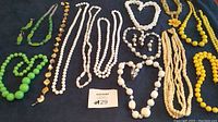 Full view of colorful costume jewelry including green, white, cream, yellow, and gold-tone necklaces and matching earrings arranged on a black background.