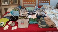 Full view of infant boy clothes, including tops, onesies, and pants laid out on table, diverse styles and colors shown.
