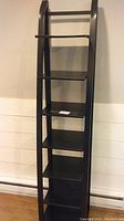 Front view of the black metal ladder-style shelving unit showing six rectangular shelves and curved side rails.
