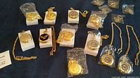 Photo showing 11 new pocket watches and 5 key chains, mostly gold-tone, some still in plastic packaging, with intricate designs.