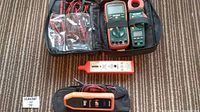 Top view photo showing multiple meters and testers in a soft carrying case and loose on carpet.