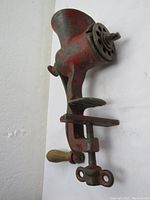 Side view of the antique red cast iron meat grinder showing clamp and wooden handle