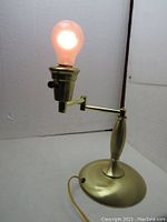 Brass colored metal table lamp turned on showing the light bulb glowing.