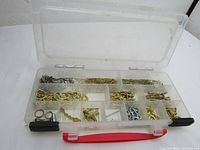 Plastic container with multiple compartments holding various small nails, hooks, and picture hanging hardware in metallic finishes.