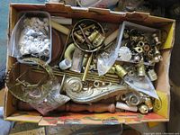 Box filled with assorted used lamp parts showing pipes, sockets, screws, and decorative metal pieces.