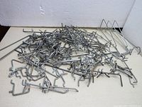Pile of various metal peg board hooks in different sizes and types, including some with multiple prongs.