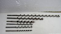 Six used wood auger bits lined out horizontally showing various sizes and spiral flutes