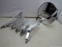 Side view of the round magnifying mirror attached to the fully retracted accordion extension arm and wall mounting plate, showing the chrome finish and construction.