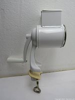 Side profile image of the assembled white enamel-coated European style nut grinder with clamp and hand crank attached showing overall appearance.