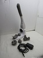 Handheld electric massager standing with six different massage head attachments displayed and a power adapter with charging cable placed in front.