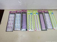 Photo showing eight new packages of self-stick glitter decorations including two from Dollarama and six from Glitterazzi in various colors and styles.