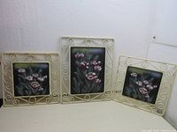 Three raised tile picture pieces displayed together showing floral designs in decorative metal frames