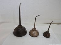 Three vintage oil can dispensers arranged side by side showing the different sizes and condition of each.