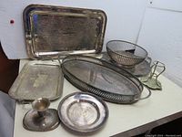 Lot of eight silver plated pieces including plates, candle holders, and bowl shown on white background.