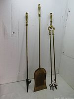 Full view of the three brass fireplace tools (shovel, poker, tongs) standing upright against a white background.