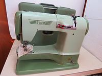 Side view of vintage ELNA Supermatic sewing machine in light green color with stitches on fabric attached.
