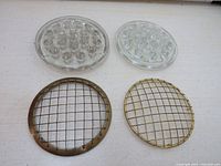 Top view of 2 glass and 2 brass vintage flower frogs laid on a light surface, showing circular holes and grid patterns.