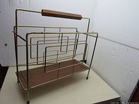 Front and side view of vintage metal and wood magazine holder showing geometric swirling metal design and wood base with wood handle on top.