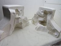 Two halves of plaster mold placed open side up, showing overall form and relief details of fairy and butterfly/shell motifs. Each half measures around 14 inches by 9.5 inches.
