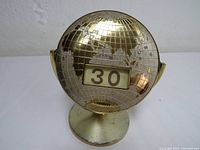 Front angled view of the metal perpetual world globe calendar showing embossed continents and date display window set to 30.