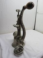 Full side view of the vintage cast iron Universal meat grinder, showing the crank handle and grinding plate removed and placed in front.