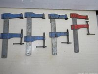 Top view of four woodworking C clamps arranged flat, three blue Speed-Master clamps and one red no-name clamp; clamps show signs of use and wear.