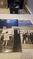 Four vinyl records displayed on a table with visible cover art showing four distinct album covers