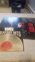 War Greatest Hits vinyl record partially on album cover with visible gold record label.