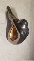 Side angle view showing the abstract human form figurine with polished metal finish and gold-toned interior cavity.
