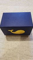 Navy blue box with yellow whale illustration on the side