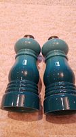 Pair of blue gradient Le Creuset salt and pepper shakers standing upright on a textured light surface, showing their full size and shape.