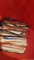 Stack of over 100 7 inch vinyl records in sleeves inside a red container.