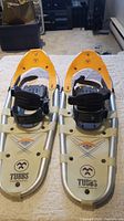 Pair of Tubbs snowshoes with aluminum frames and yellow pointed toe caps placed side by side.