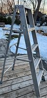 Side view of the 5 foot aluminum fold-up ladder standing on a wooden surface outside with snow in the background.
