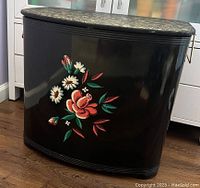 Front view of black curved hamper with colorful hand-painted floral design on the front surface.